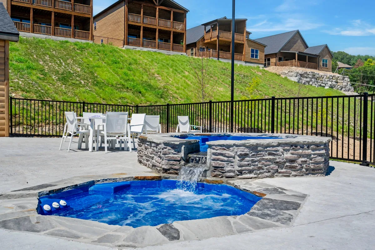 Multiple hot tubs are situated on a spacious outdoor patio overlooking a landscaped hillside. An outdoor dining set invites guests to enjoy meals or morning coffee with a view. The mood is serene and leisurely, perfect for group gatherings or quiet moments.