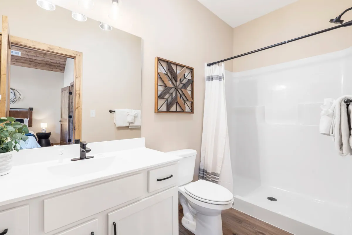 A modern bathroom space featuring a sleek vanity with a large mirror, geometric wall art, and a walk-in shower area. The setting feels fresh and tranquil, designed for relaxation and rejuvenation after a day of activity.