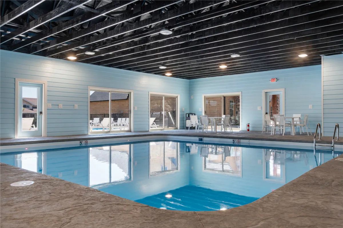 A tranquil indoor pool area with large windows that flood the space with natural light. Comfortable seating is arranged along the poolside, encouraging both relaxation and socializing in a climate-controlled environment. The atmosphere is calm and refreshing, perfect for year-round enjoyment.