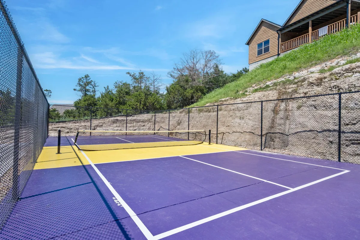 A lively exterior view of a tennis court set amid greenery with a house in the background. The scene captures the energetic mood of guests enjoying a friendly match, surrounded by nature and resort accommodations.