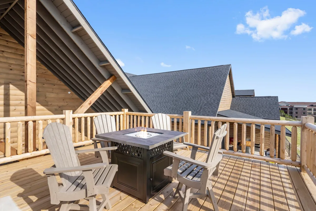An inviting fire pit surrounded by wooden chairs sits on a deck with a mountain view. The setup encourages evening gatherings, socializing, and enjoying the outdoors under the stars.