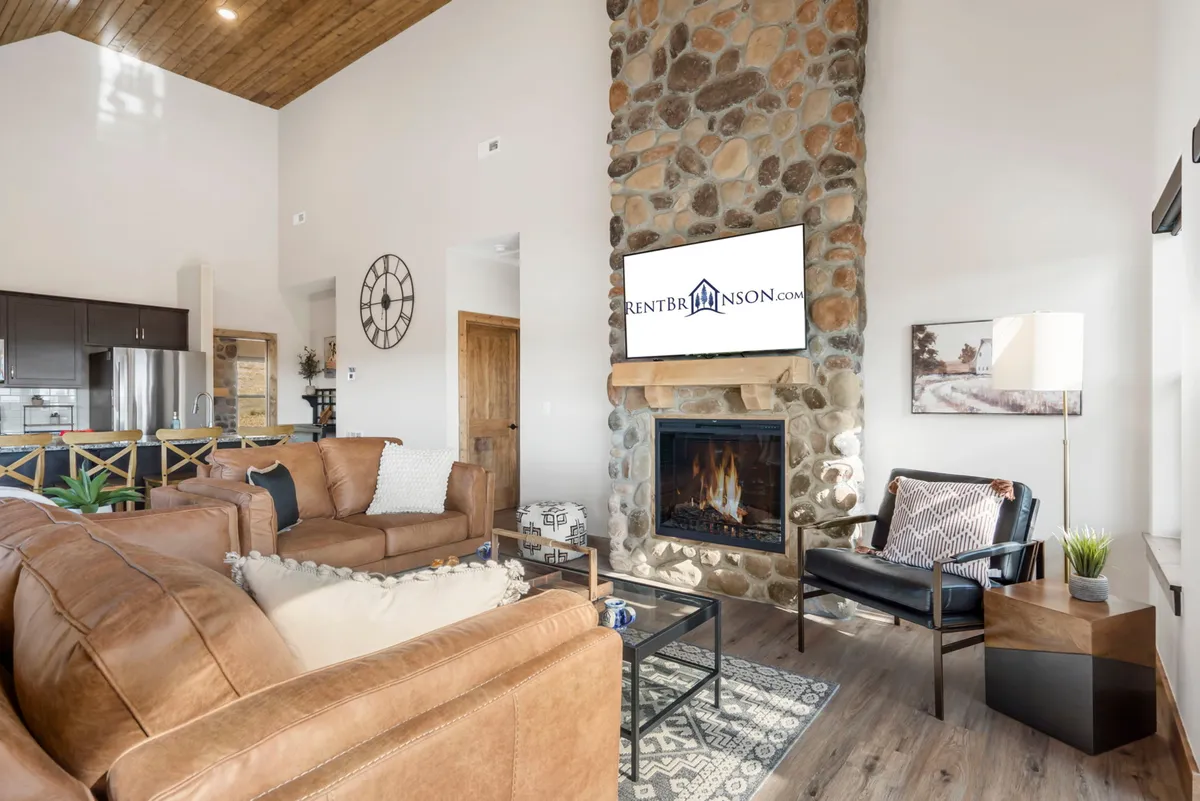 A comforting living space with a stone fireplace, rich leather sofa, TV mounted above the hearth, decorative lighting, and a soft area rug. The room feels intimate yet spacious, inviting guests to relax, converse, or enjoy entertainment together.