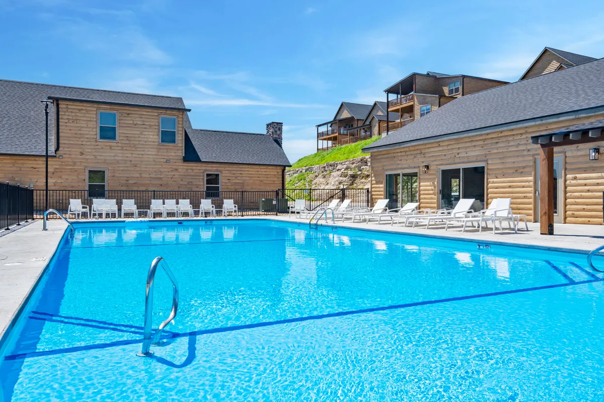 This exterior image captures a large swimming pool surrounded by lounge chairs, with wooden buildings and a landscaped hillside in the background. The scene suggests opportunities for swimming, sunbathing, and relaxed socializing, and is set against a backdrop of natural beauty, hinting at the enjoyable summertime atmosphere.