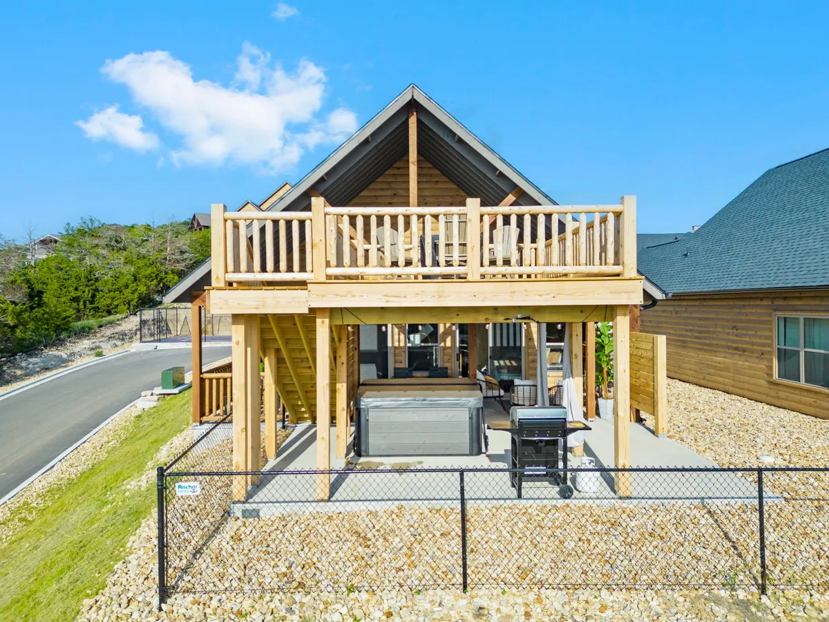 A spacious wooden deck features a bubbling hot tub, a grill, and comfortable seating, all overlooking a serene landscape. The setting is perfect for unwinding, stargazing, or sharing a sunset together in the warmth of the tub.