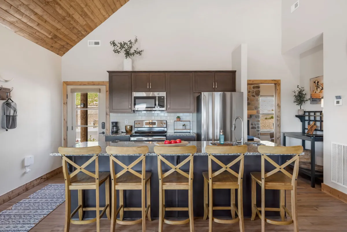 A modern, open kitchen with a central island, high-quality cabinetry, stainless appliances, and dining stools, all under a warm wood plank ceiling. The space feels bright, welcoming, and designed for both cooking and socializing.