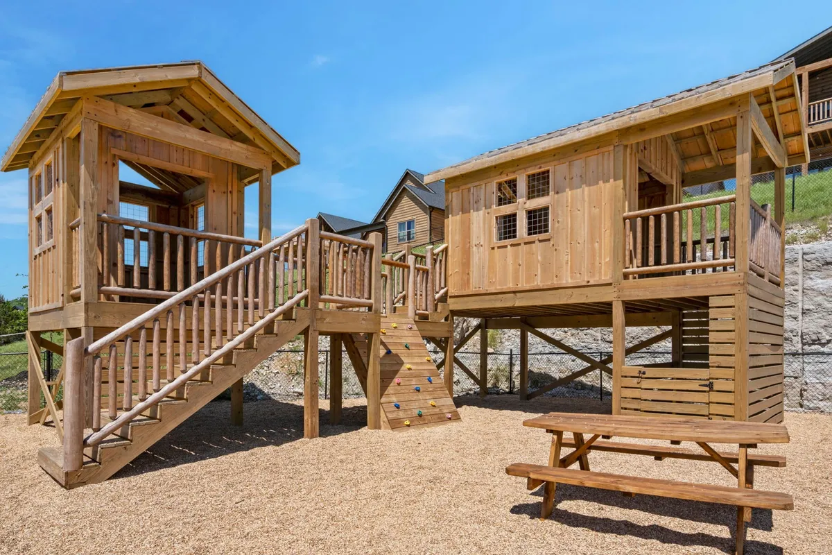 A vibrant outdoor play structure featuring a climbing wall and picnic table sits nestled in green surroundings, inviting children to play and families to picnic together. The joyful mood and visible play equipment perfectly match the community playground mentioned in the section.