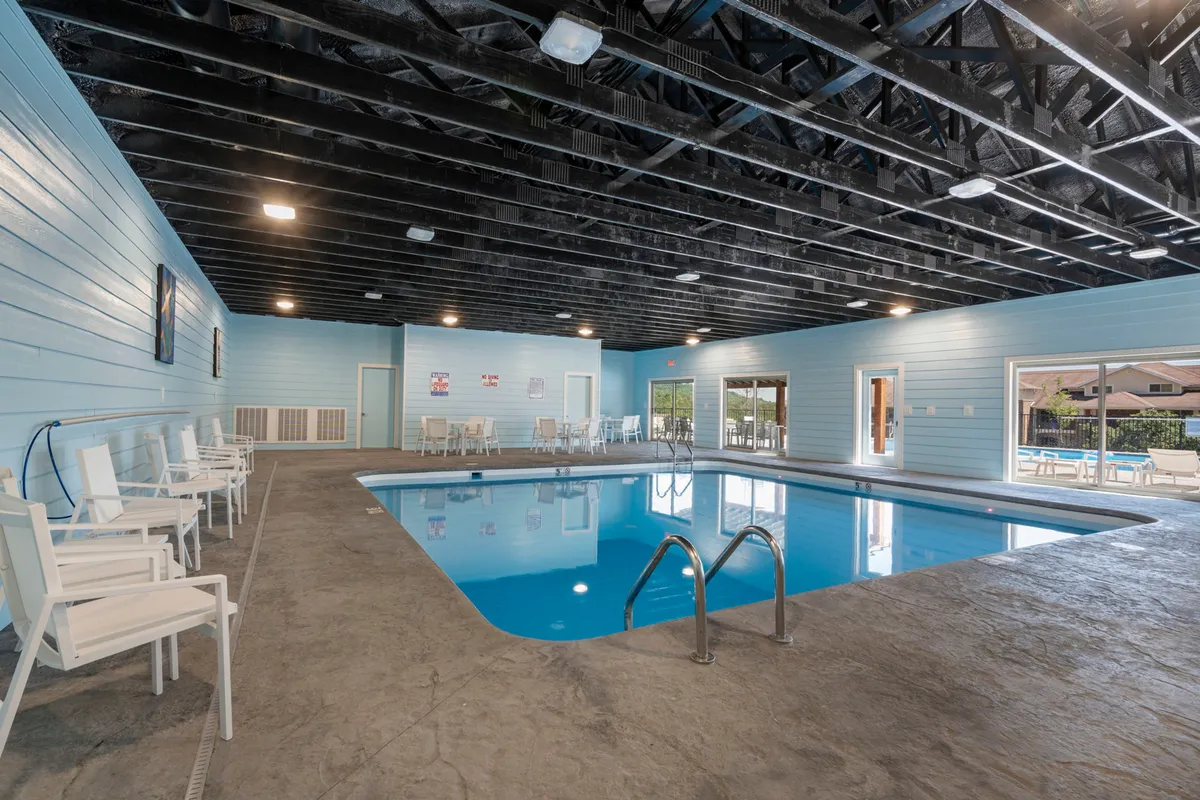 The interior of the resort's indoor swimming pool area, featuring a spacious pool, large windows that let in natural light, white chairs for lounging, and painted blue walls. The space feels calm and inviting, offering a retreat regardless of weather or season.